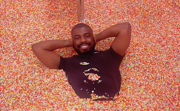 Me in a pit full of plastic sprinkles with my hands behing my head smiling